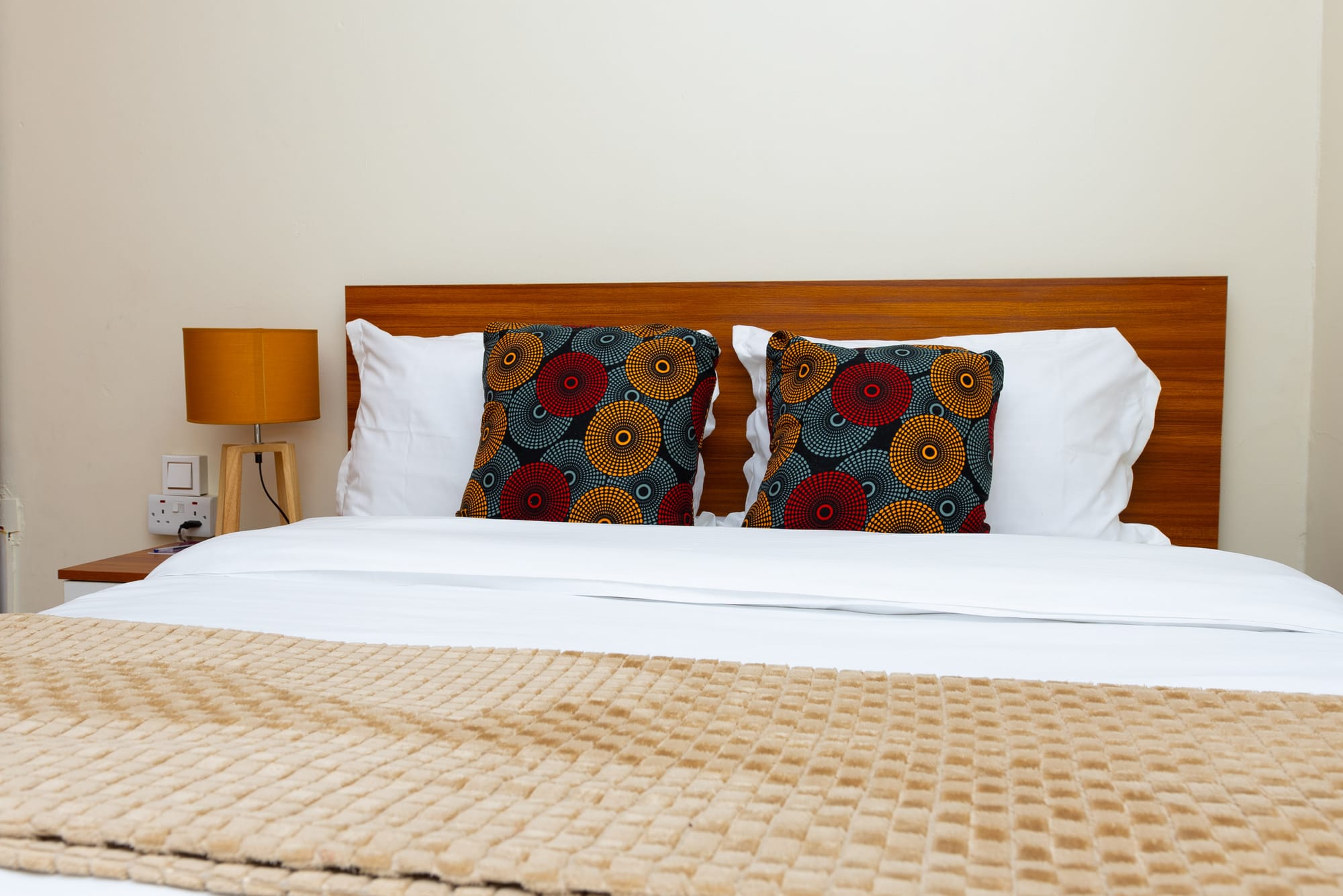 A guest room bed dressed in white with bold African print cushions and a woven throw