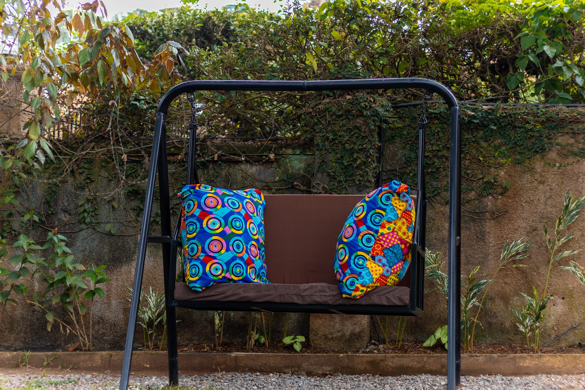 A garden swing seat with bright African print cushions set against a leafy living wall