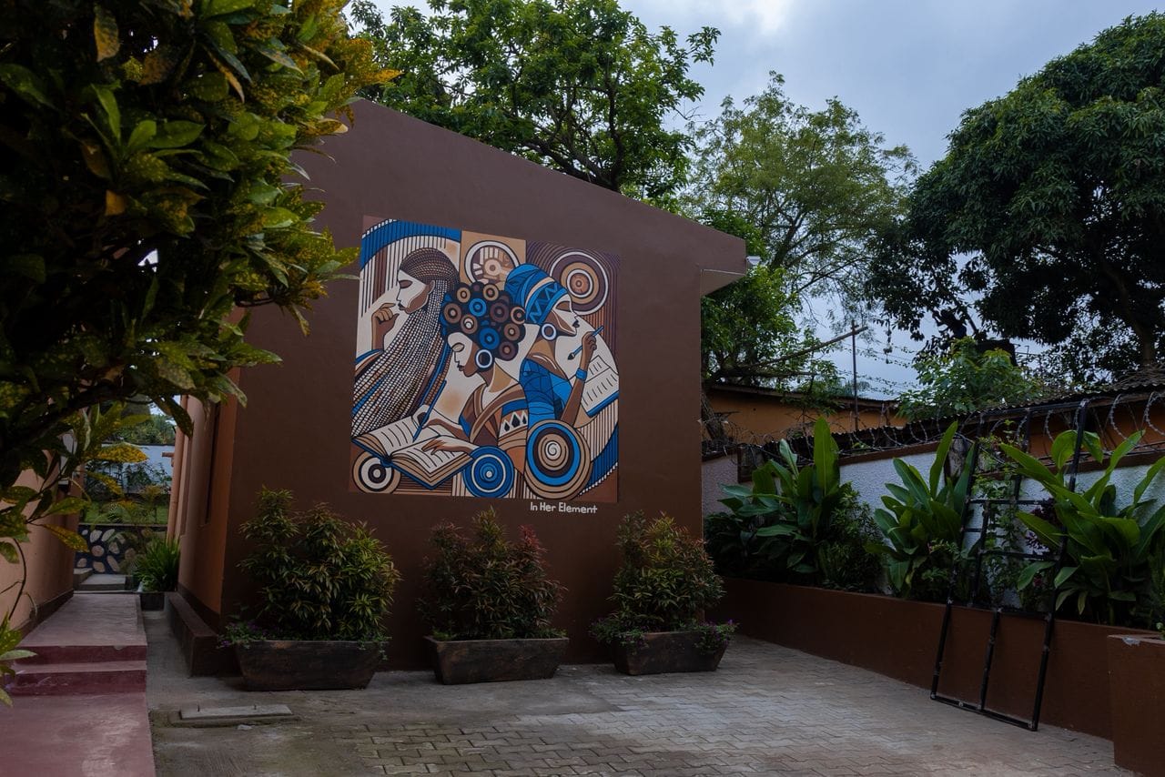 KaraSpace B&B with the In Her Element mural on a maroon wall, framed by greenery