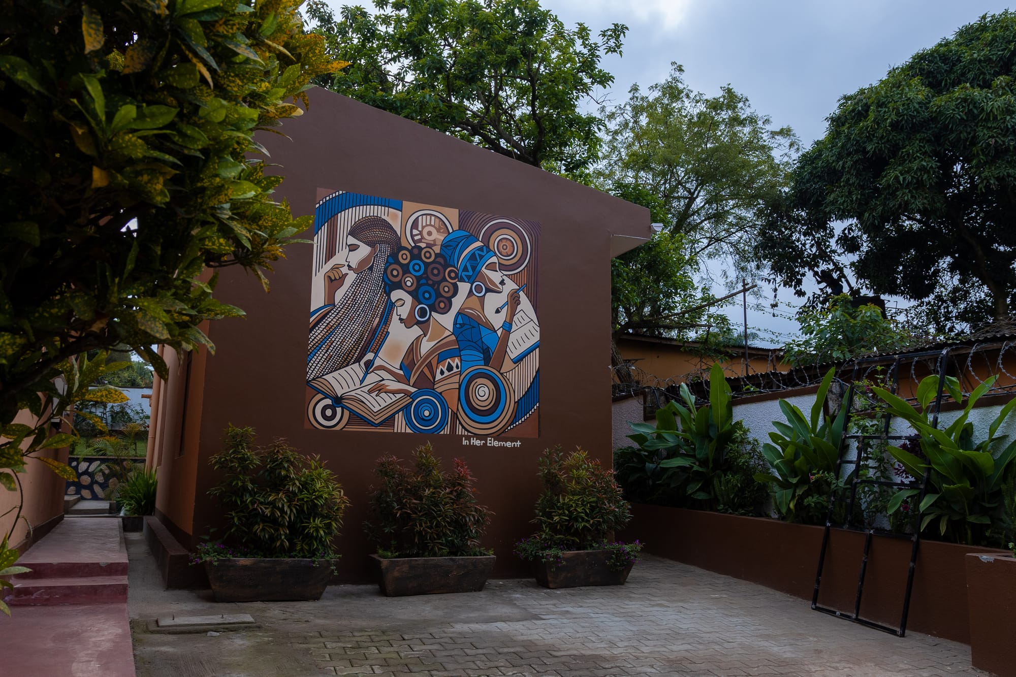 The In Her Element mural on the warm brown wall of KaraSpace B&B, framed by potted plants