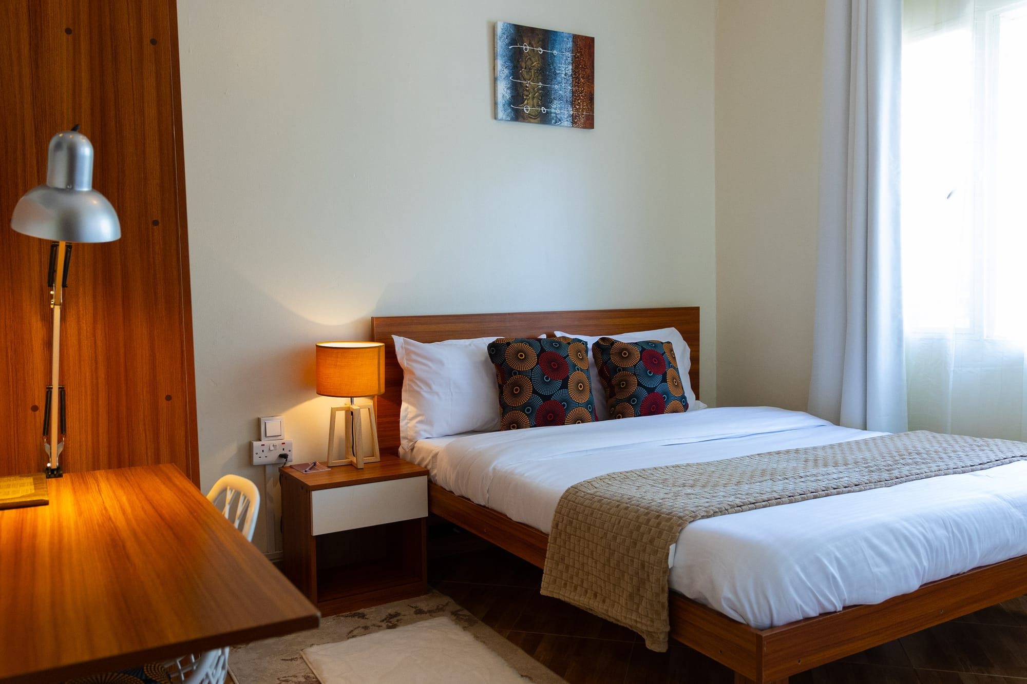 A guest room with a wooden writing desk, reading lamp and a neatly made bed