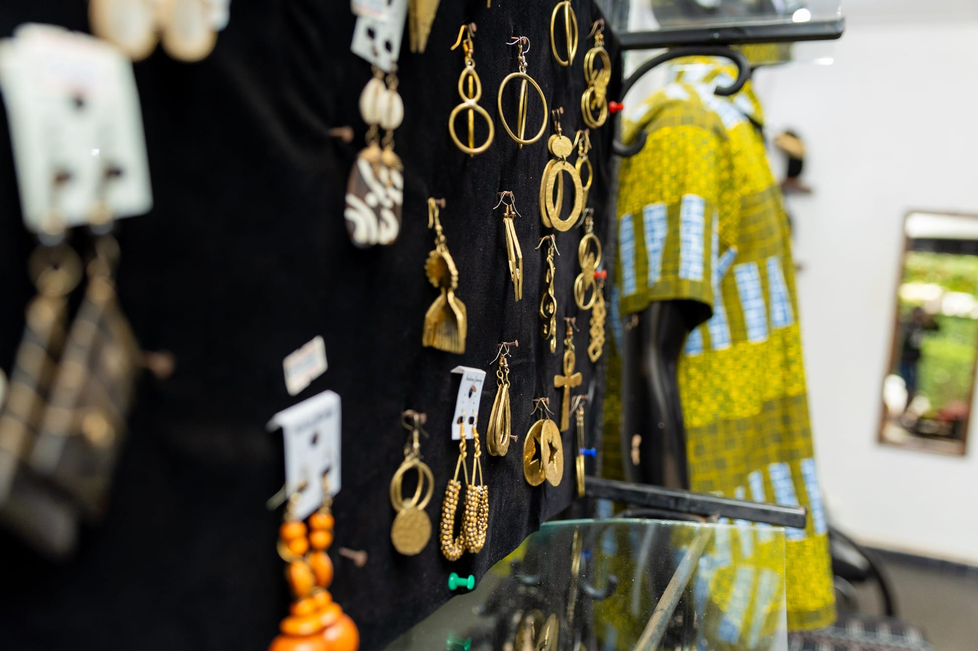 A wall of handmade brass earrings beside an African print dress on a mannequin in the KaraSpace boutique