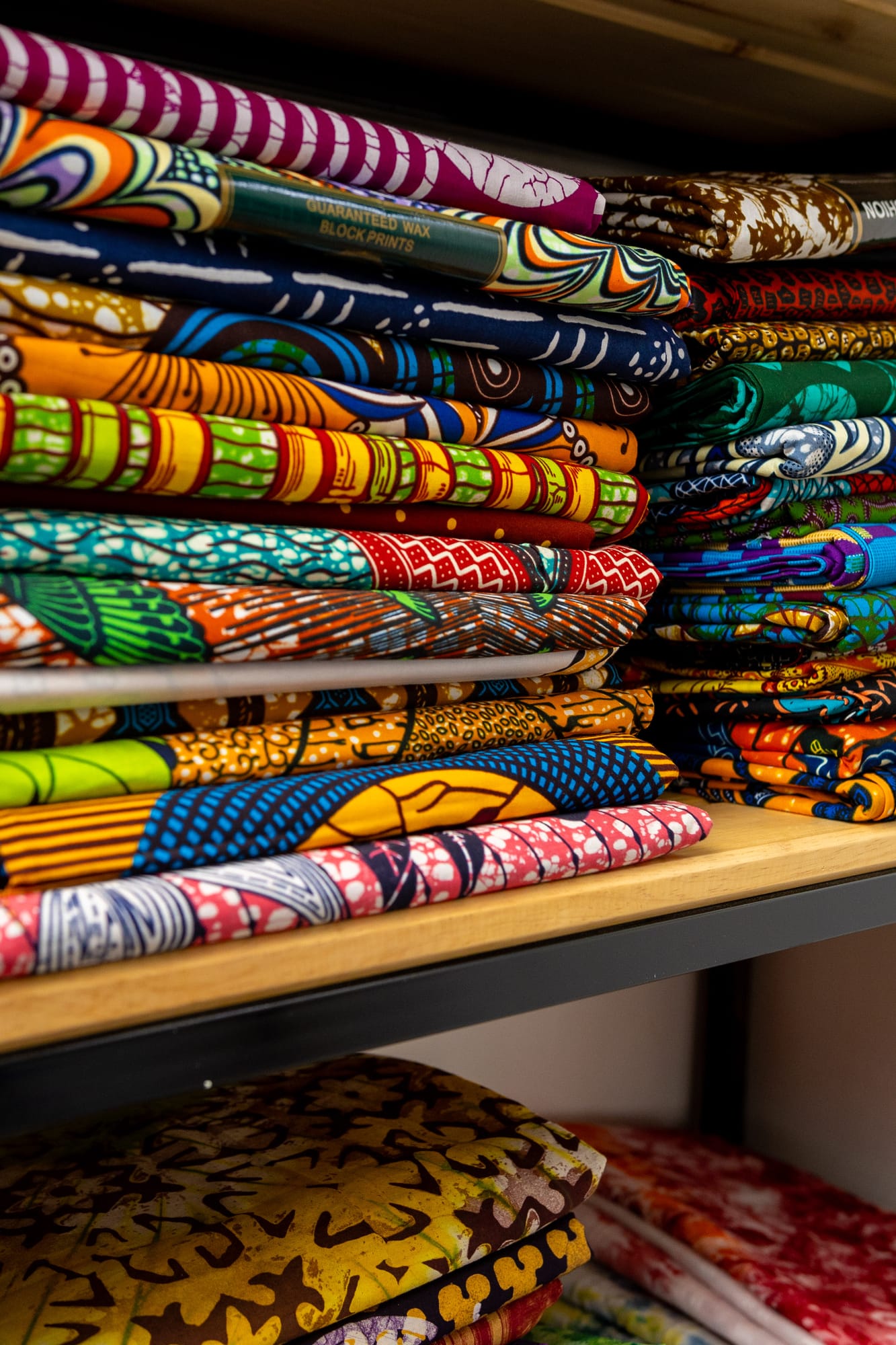Neatly folded stacks of colourful African wax-print fabrics on a shelf