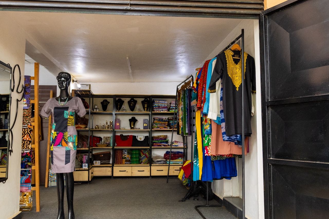 The KaraSpace boutique interior — a mannequin in an African print dress, shelves of jewellery and fabrics, and a rail of bright African garments