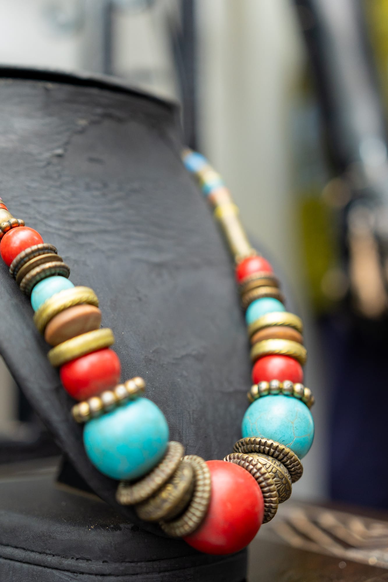 A statement necklace of turquoise, coral-red and brass beads on a black display bust