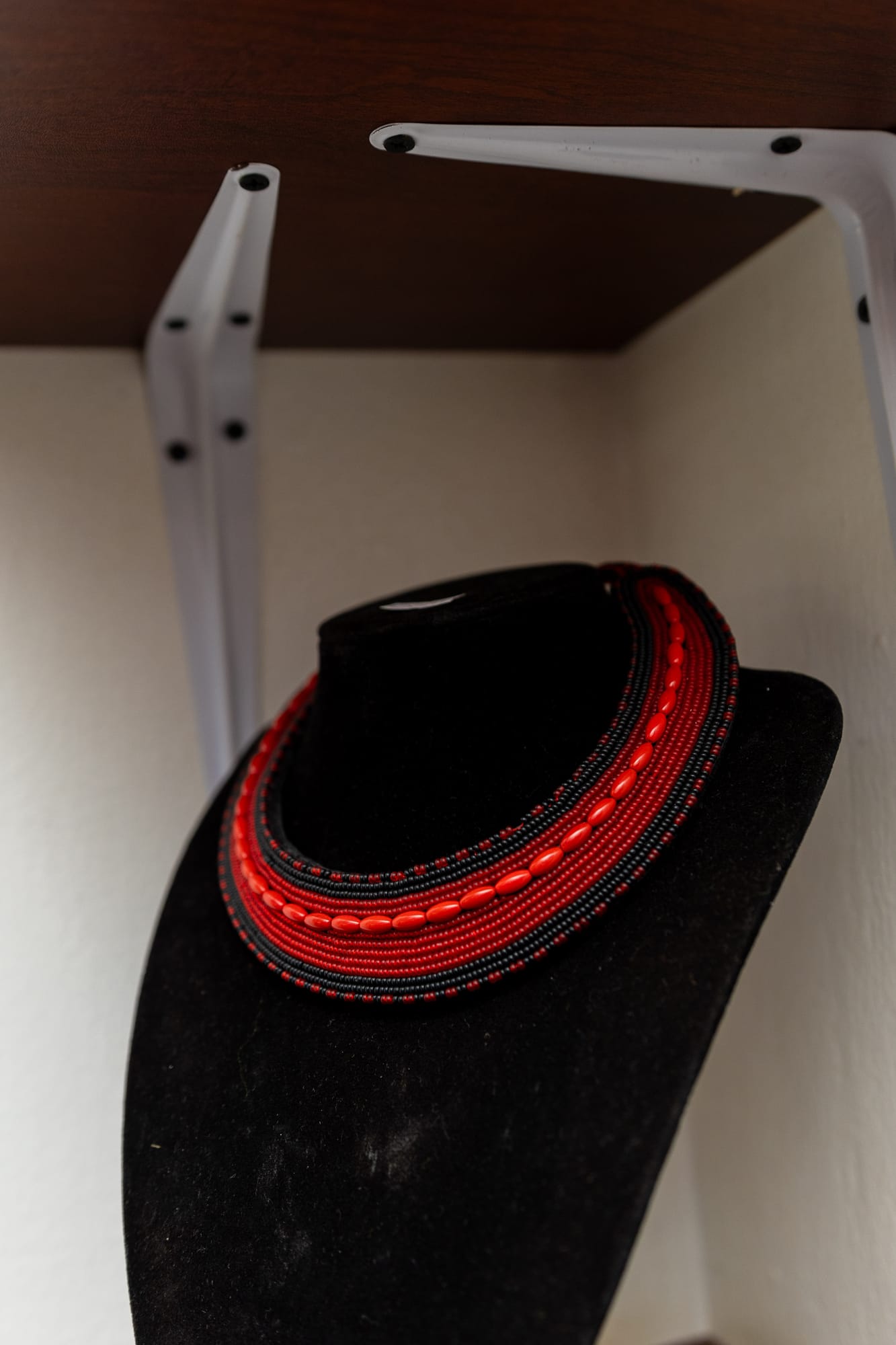A red and black beaded Maasai collar necklace on a black stand