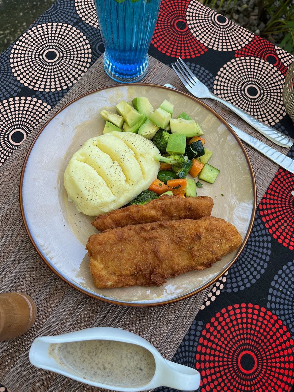 A plate of crumbed fish, mashed potato and fresh vegetables on an African print table at the KaraSpace garden café