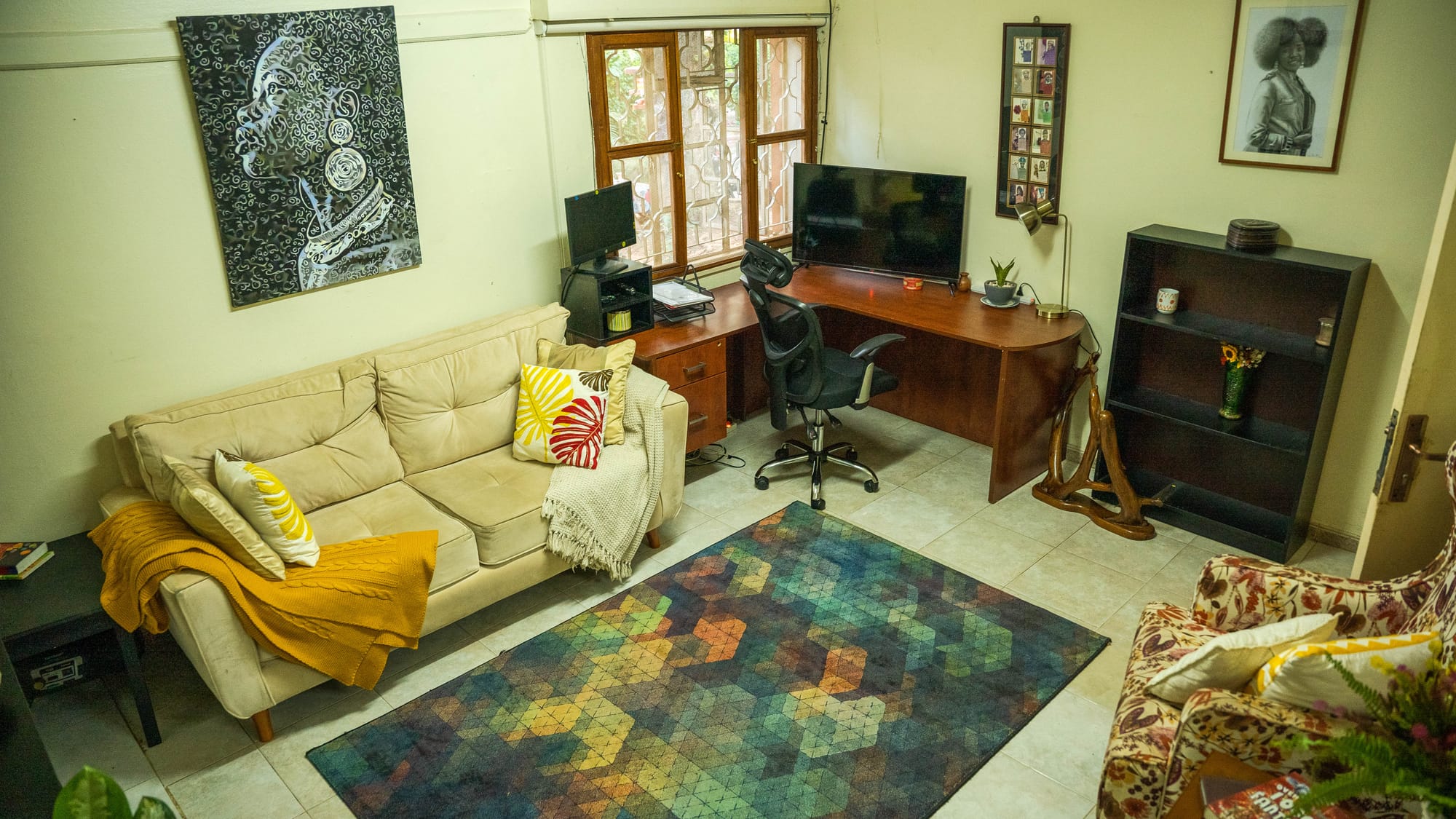 A quiet work corner — an L-shaped wooden desk with a screen and ergonomic chair on a patterned rug, beside a sofa