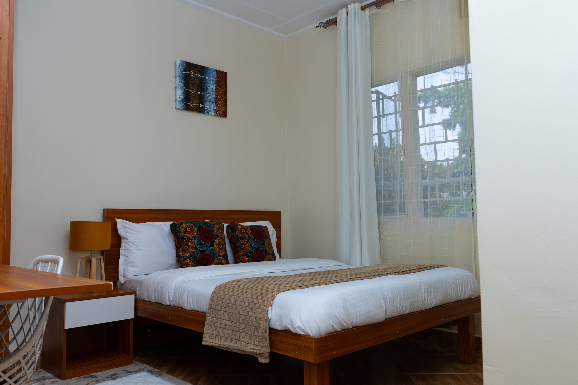 Deluxe Room — a double bed with African print cushions beside a bright window with garden views