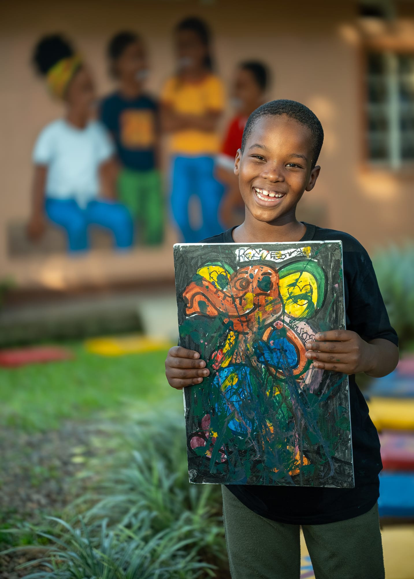 A laughing young maker in the KaraSpace garden holding up the bold abstract canvas he just painted