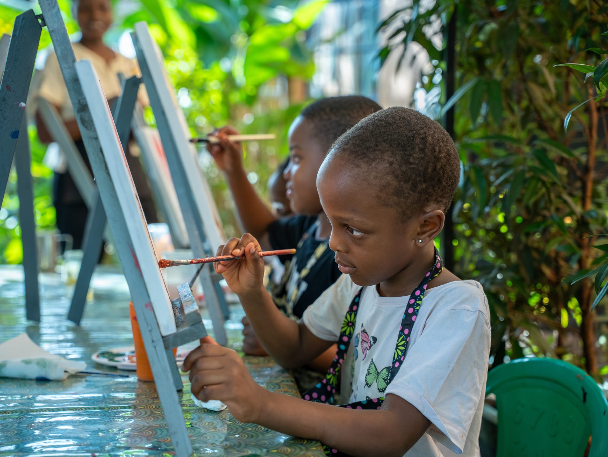 A row of easels under the trees at a Kara Paints children's session