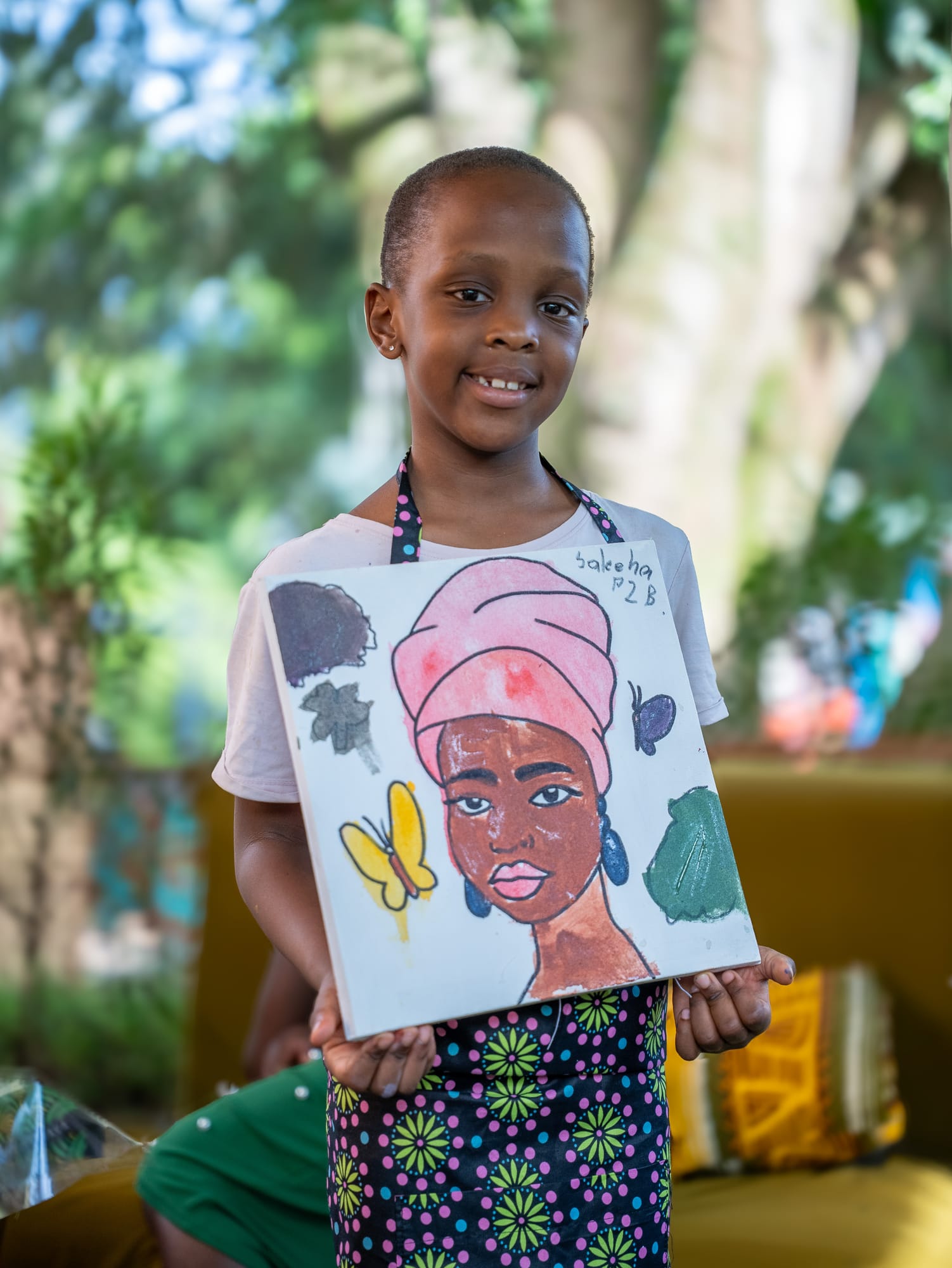 A young painter holding her portrait of a woman in a pink head wrap