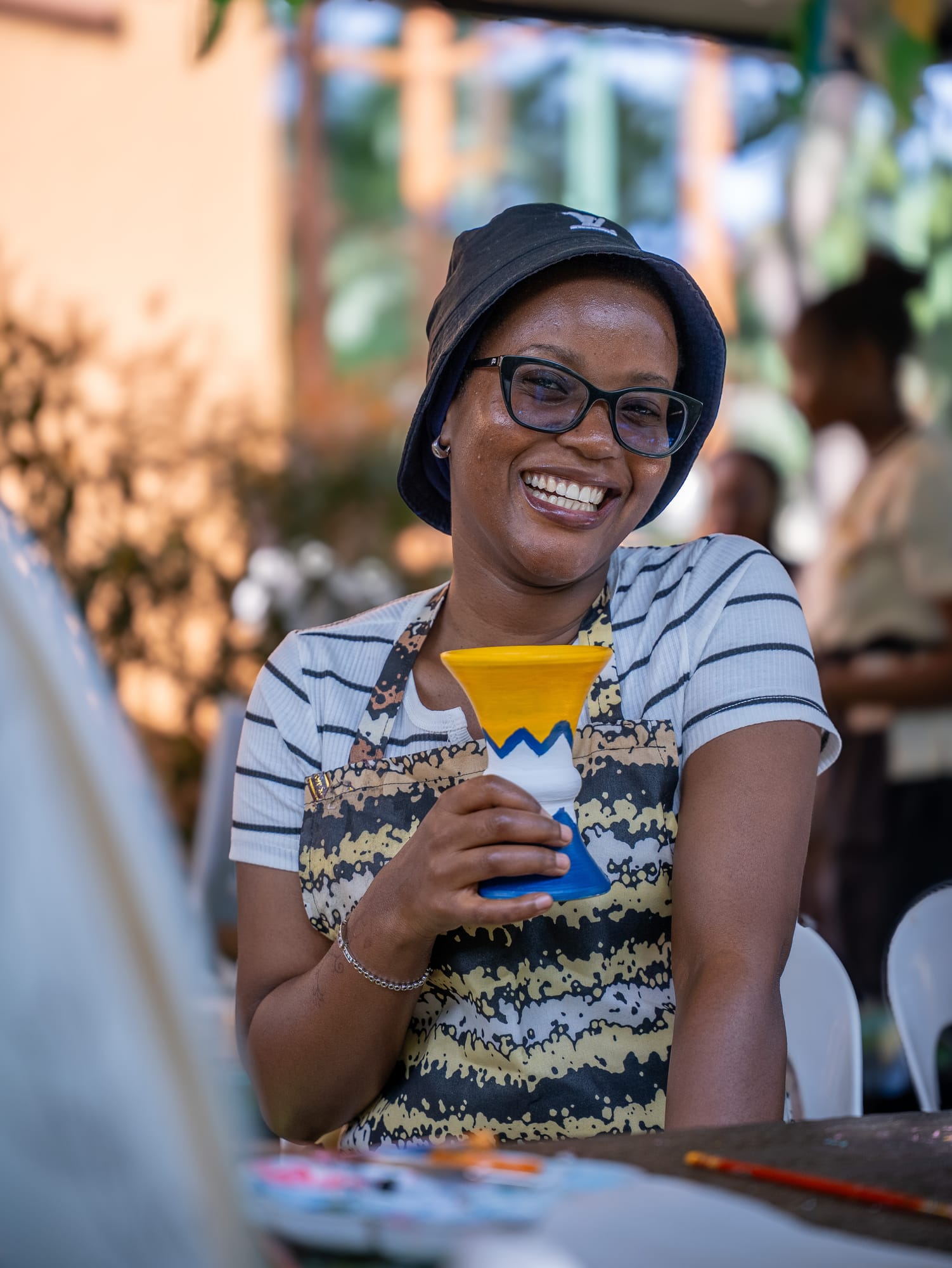 A maker smiling and holding up the blue cup she painted