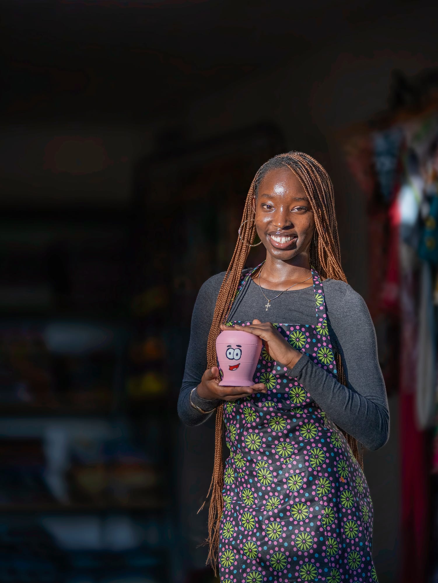 A maker in an African print apron holding the pink, smiling cup she painted