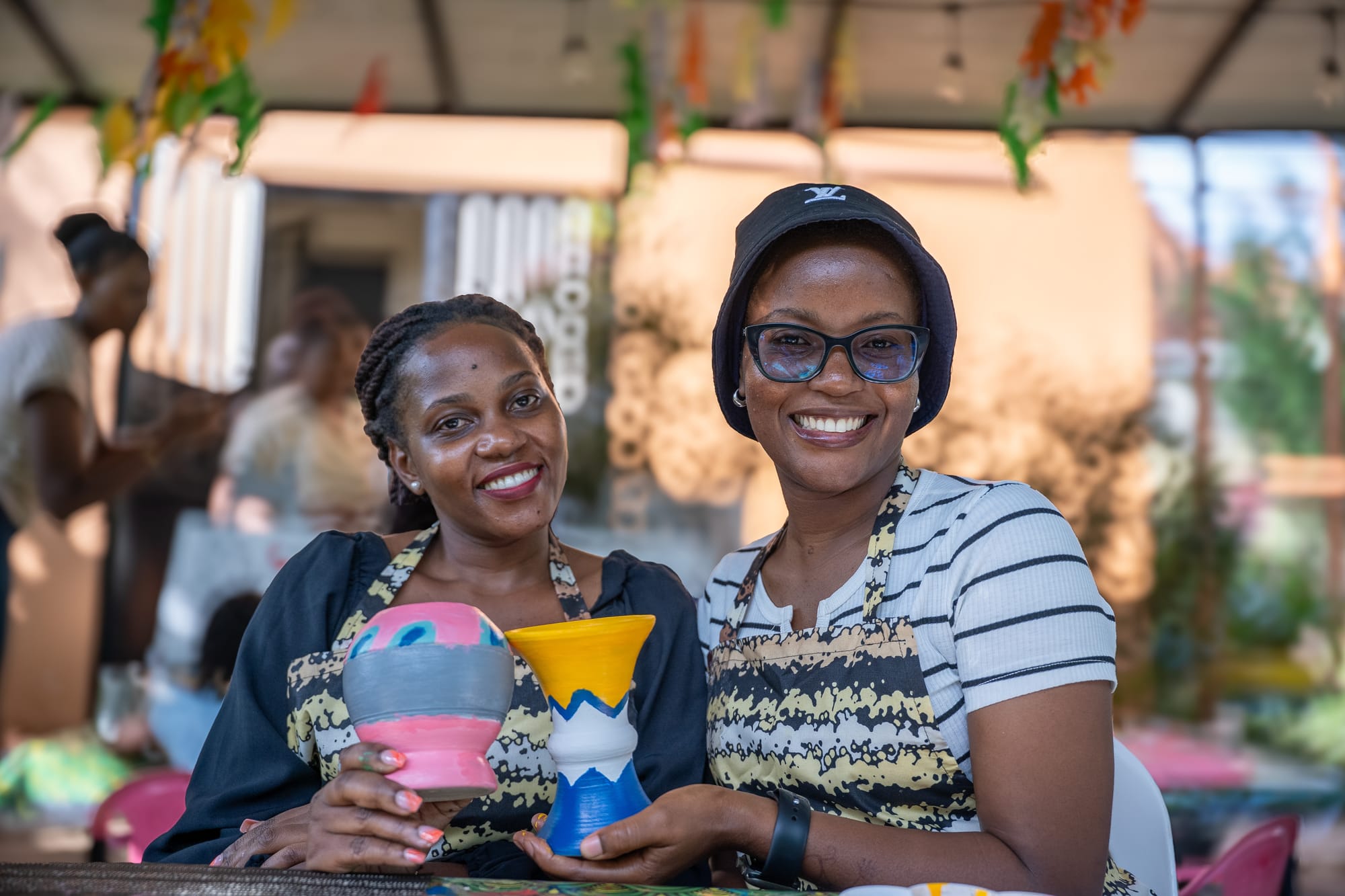 A maker smiling over the pink and grey bowl she painted, garden light behind her