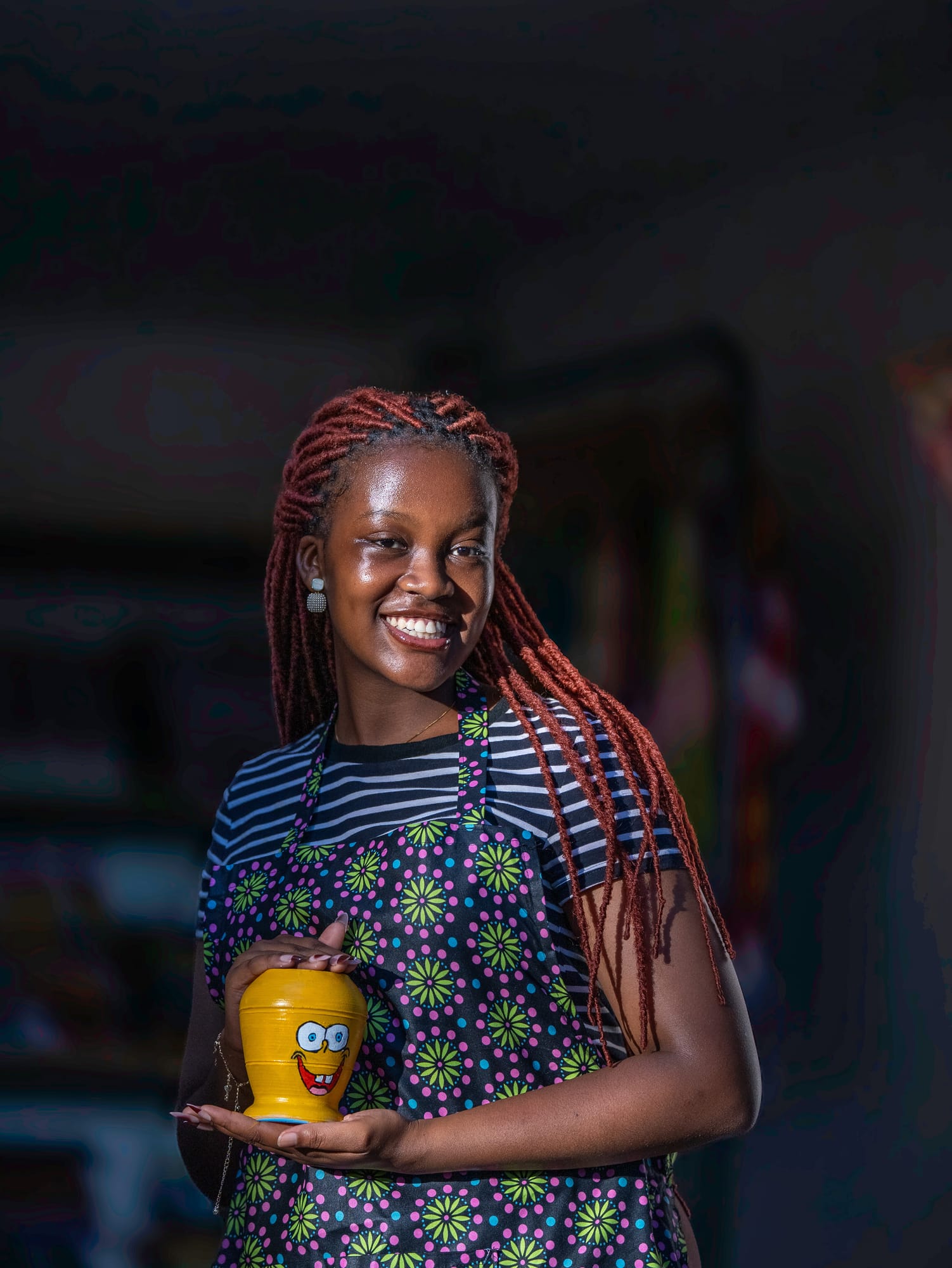 A maker holding the bright yellow, grinning cup she painted