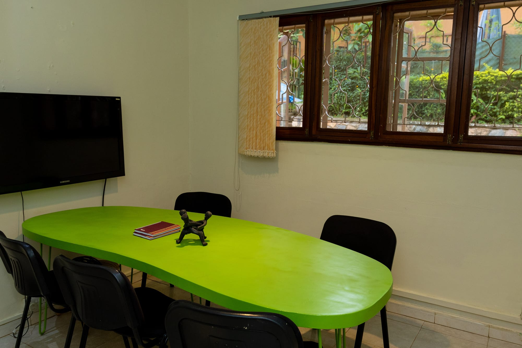 The KaraSpace meeting room — a green oval table with black chairs, a wall-mounted screen and garden views through the windows
