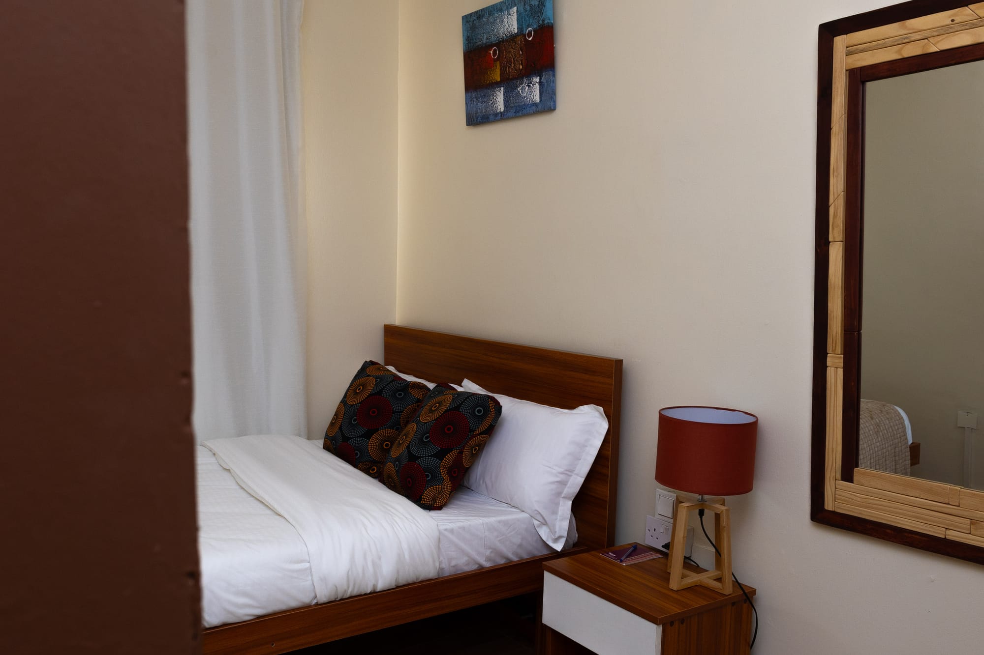 Standard Room — the made bed with a framed mirror and abstract art