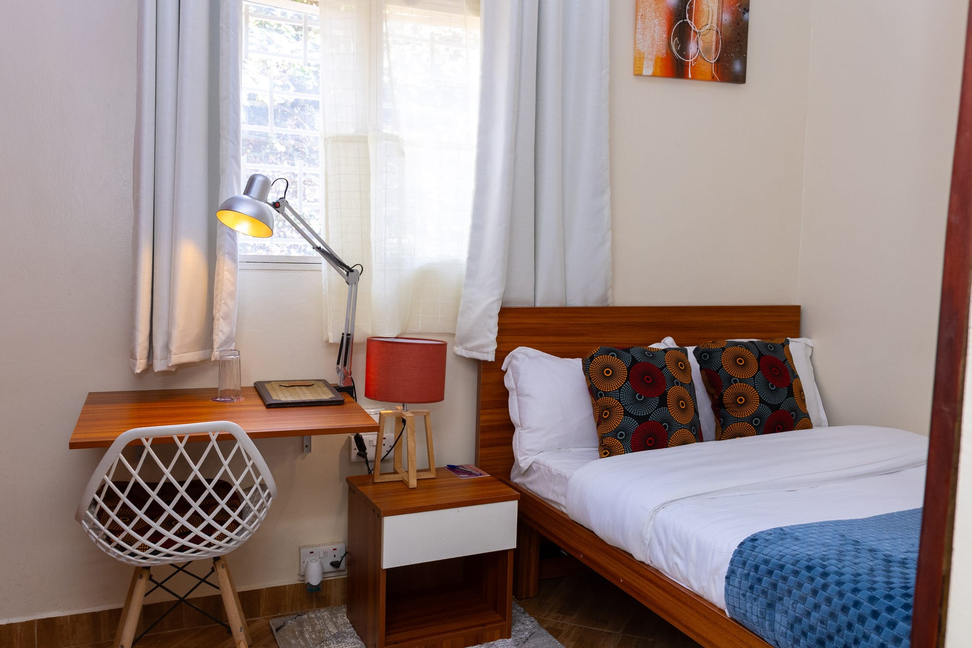 Standard Room — a single bed with African print pillows beside a wooden writing desk and window