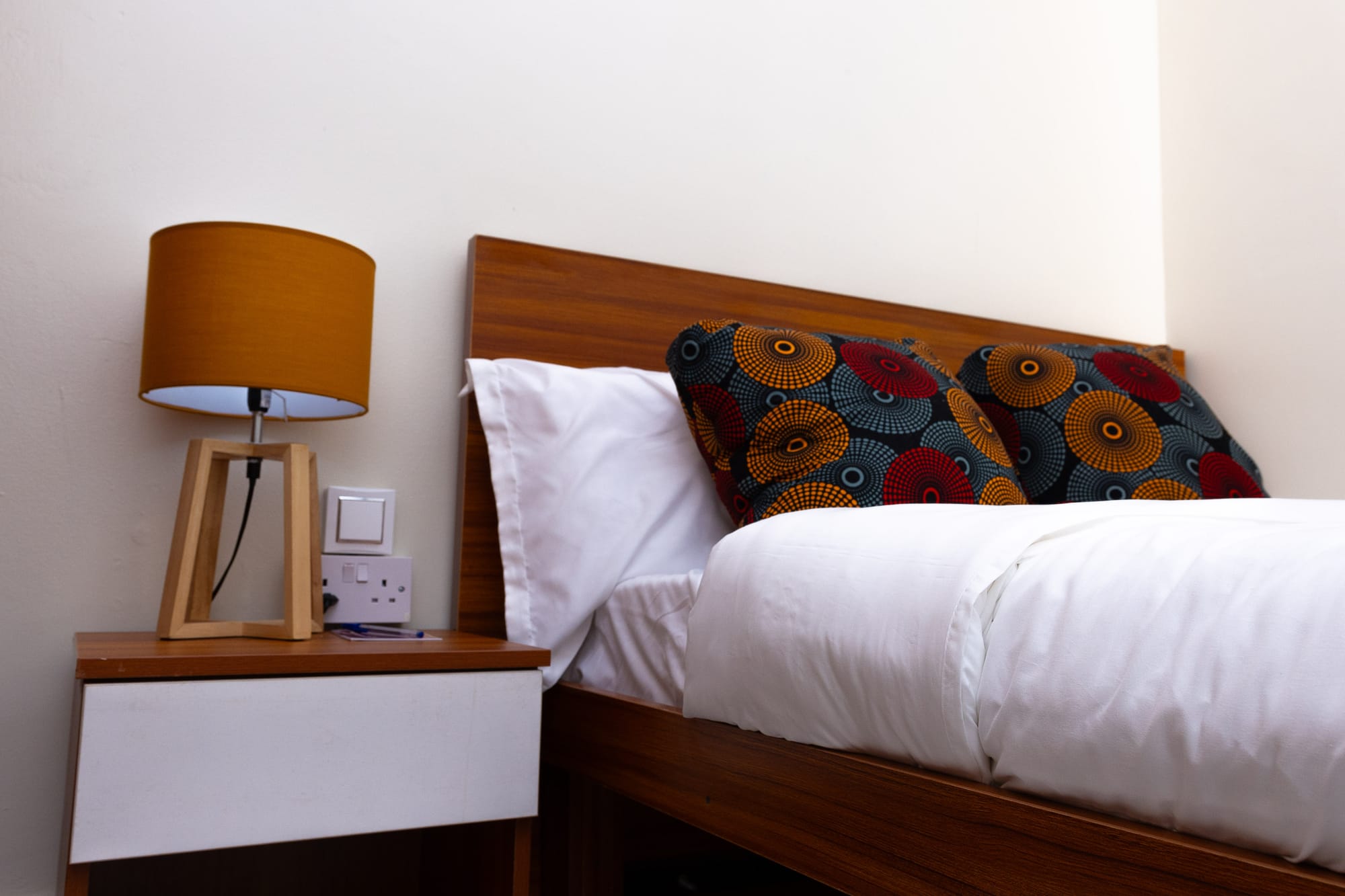 Standard Room — the wooden headboard with bold African print cushions and a reading lamp