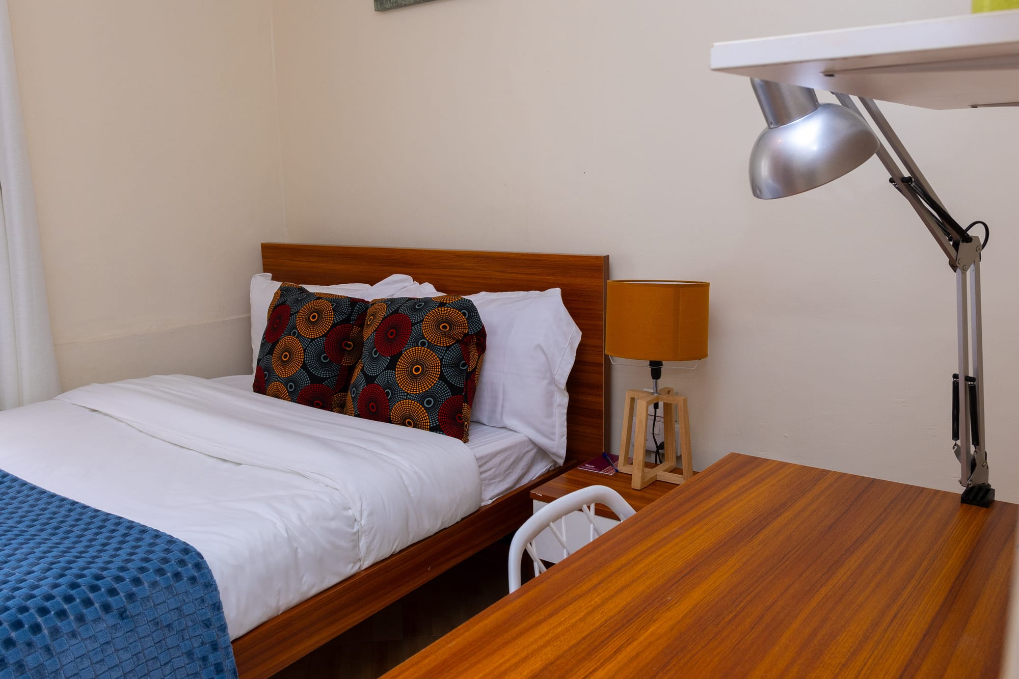 Standard Room — the bed with African print cushions beside a wooden desk and reading lamp