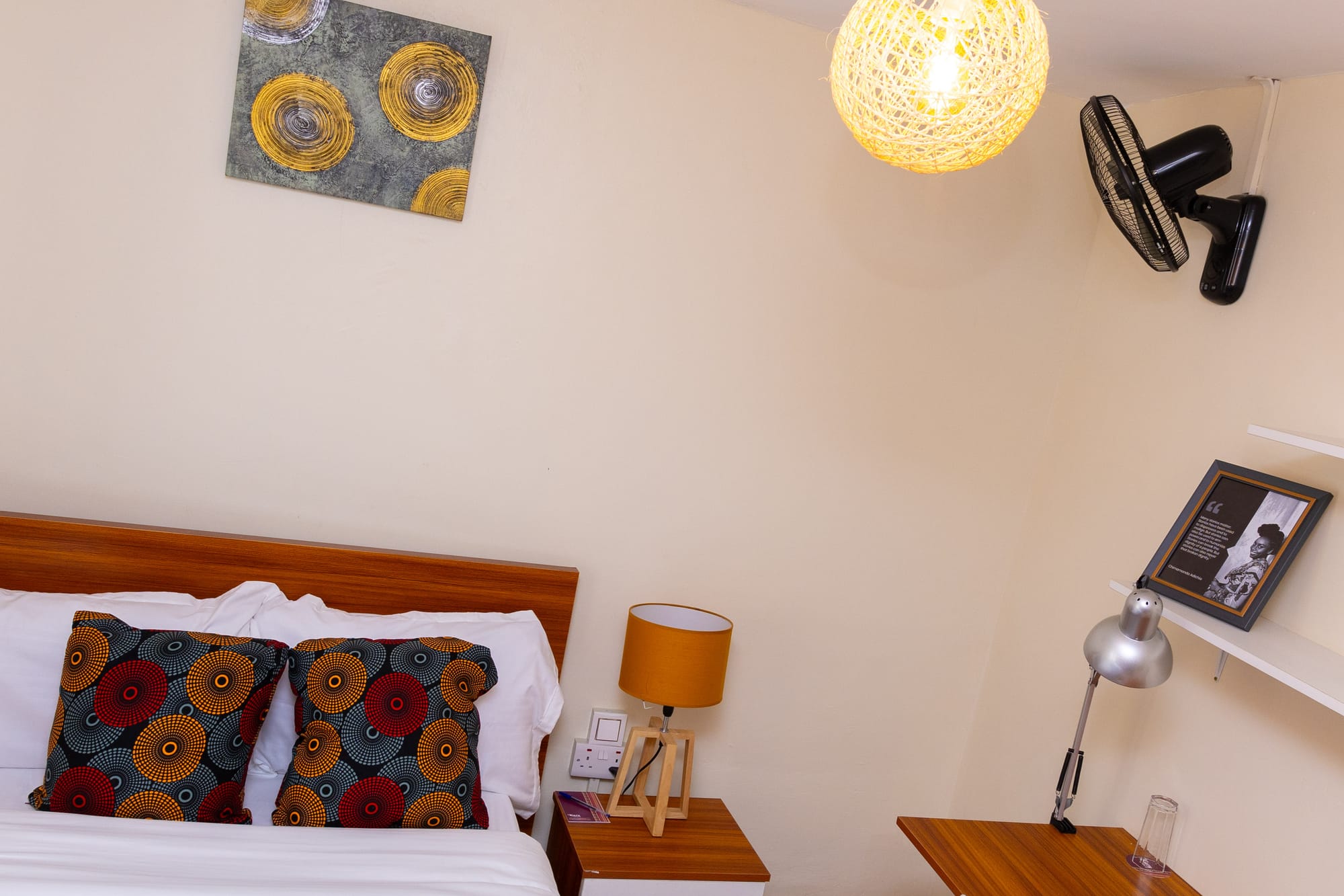 Standard Room — the headboard with African print cushions, wall fan and framed quote